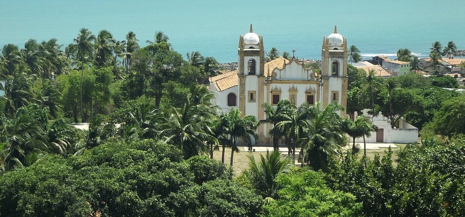 Imagem de uma igreja em frente ao mar e próxima de uma vegetação